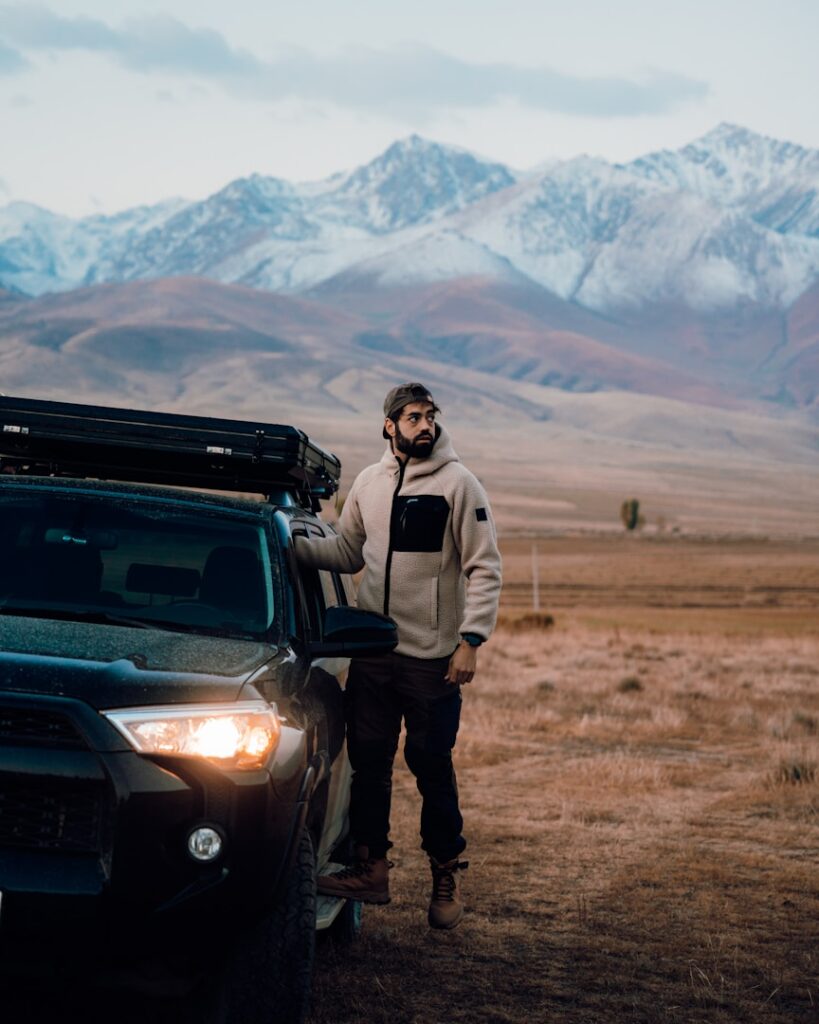 Man standing by car with snowy mountains behind