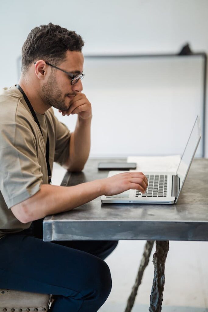 A man intensely focused on typing on a laptop in a modern office setting.
