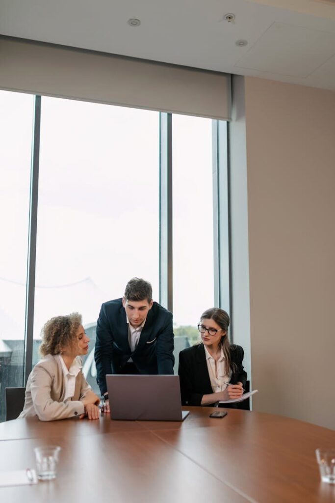 Business professionals engaged in a meeting around a laptop in a modern office setting.
